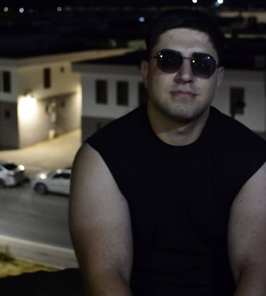 Murat Said Doğan, gece çekilmiş bir portrede güneş gözlüğü ve siyah kolsuz tişörtle kameraya bakıyor